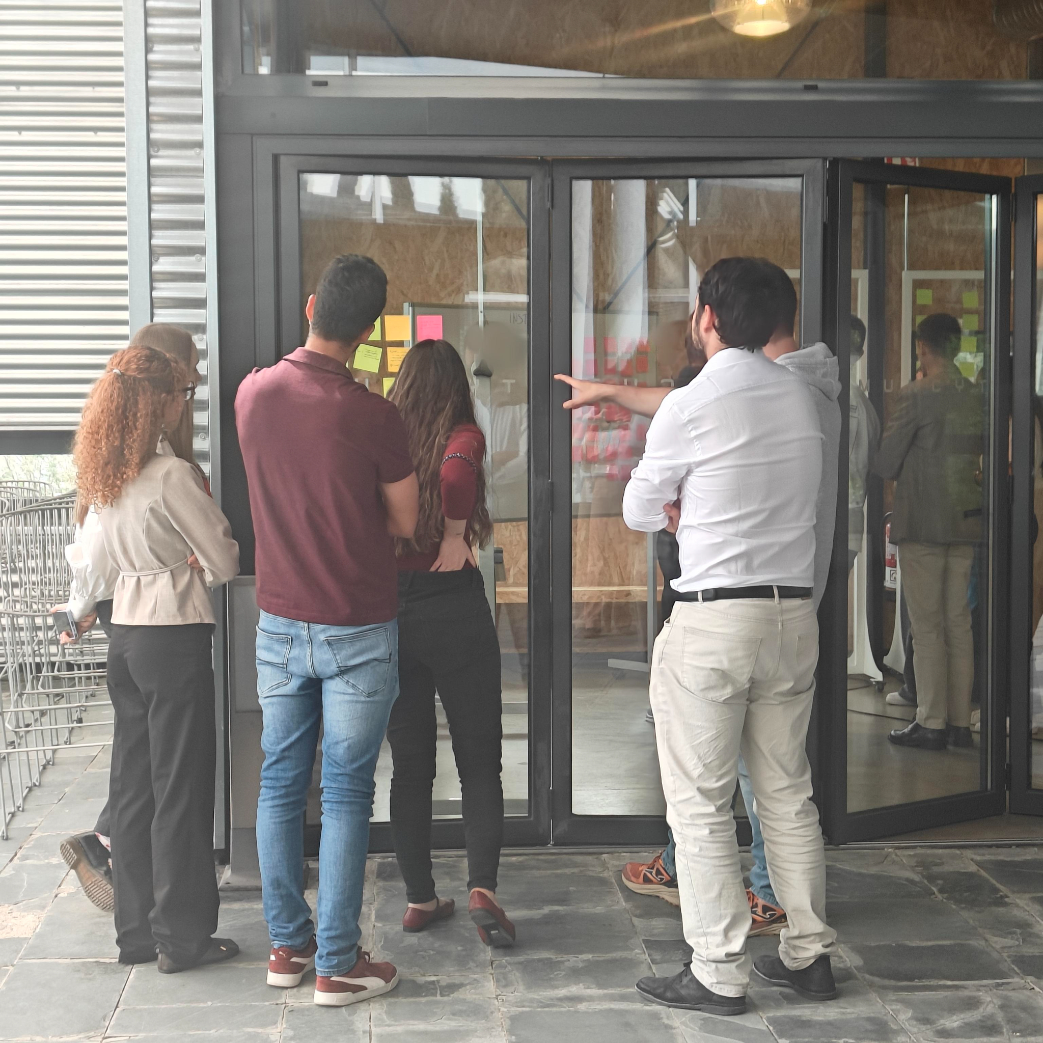 Un grupo de cinco personas trabajan en grupo alrededor de una ventana donde hay pegadas notas adhesivas.