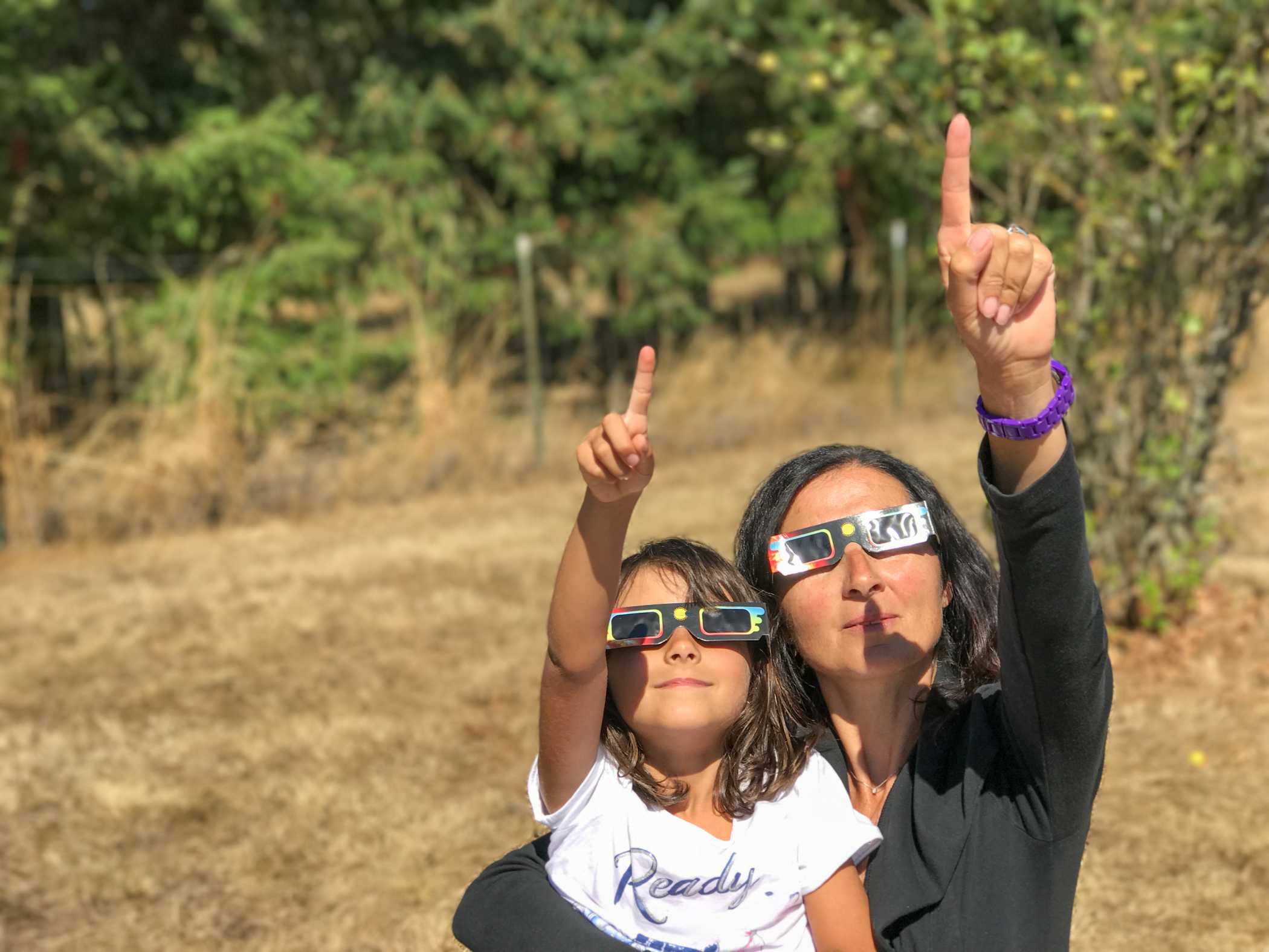 Mujer y niña observan un eclipse solar equipadas con las gafas necesarias para ello.