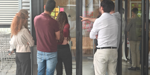 Un grupo de cinco personas trabajan en grupo alrededor de una ventana donde hay pegadas notas adhesivas.