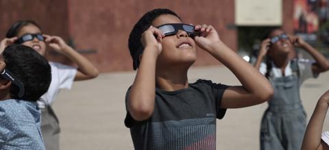 Estudiantes mirando hacia el cielo con las gafas para observación de eclipses.